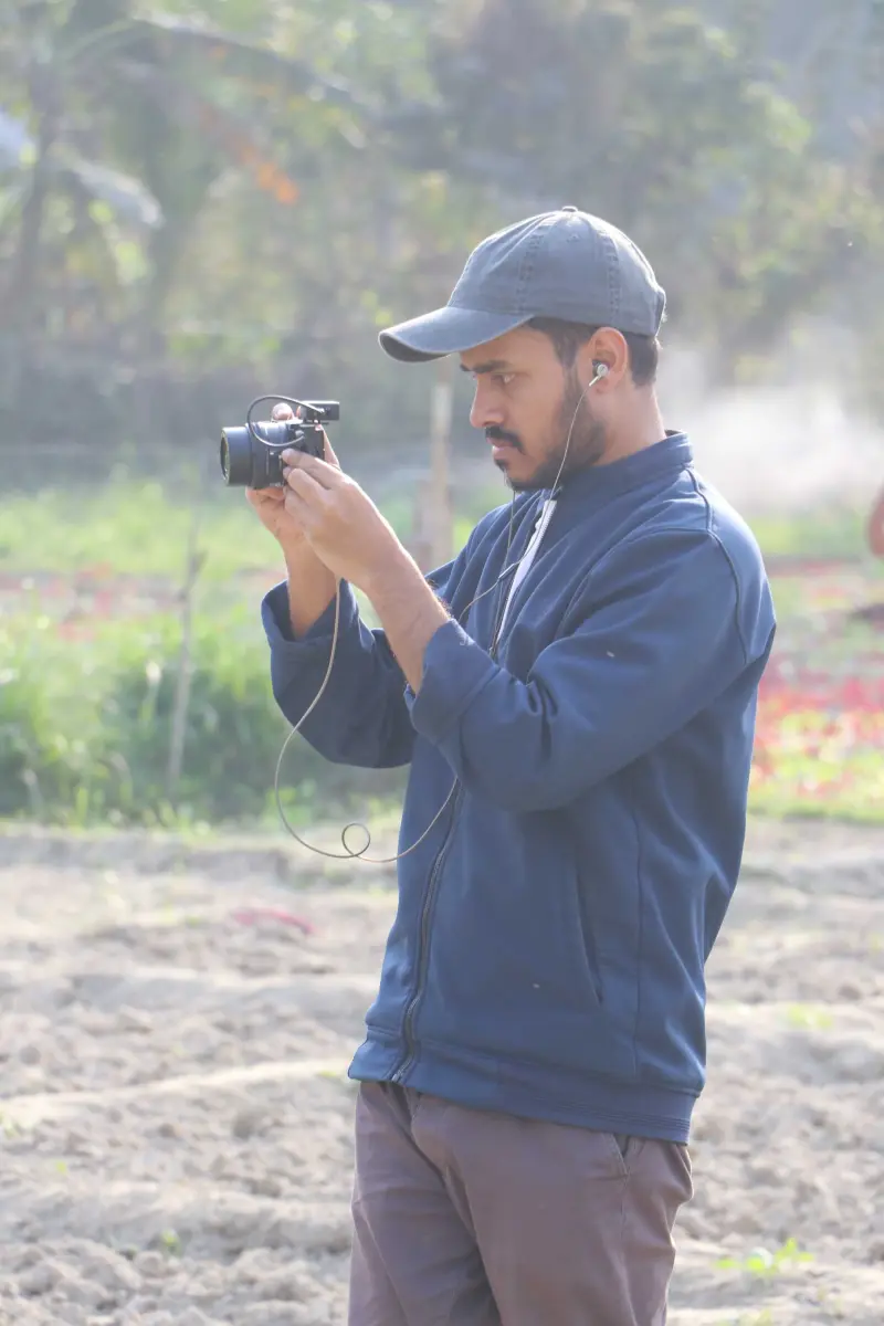 Portrait of Riaz Uddin holding a camera in a field